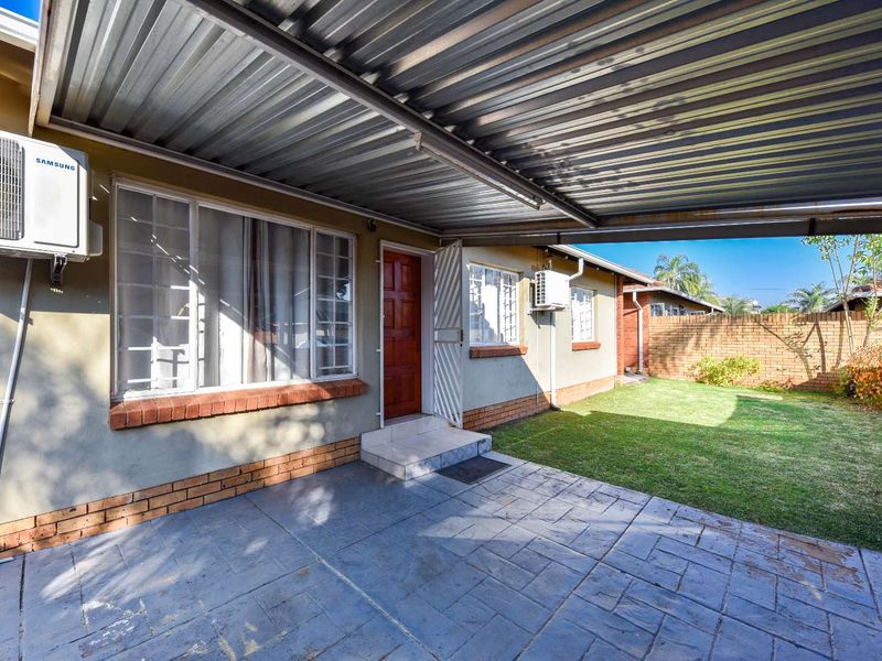 A covered patio area featuring a stamped concrete floor, corrugated metal roofing, and direct access to a small private garden with brick boundary walls.
