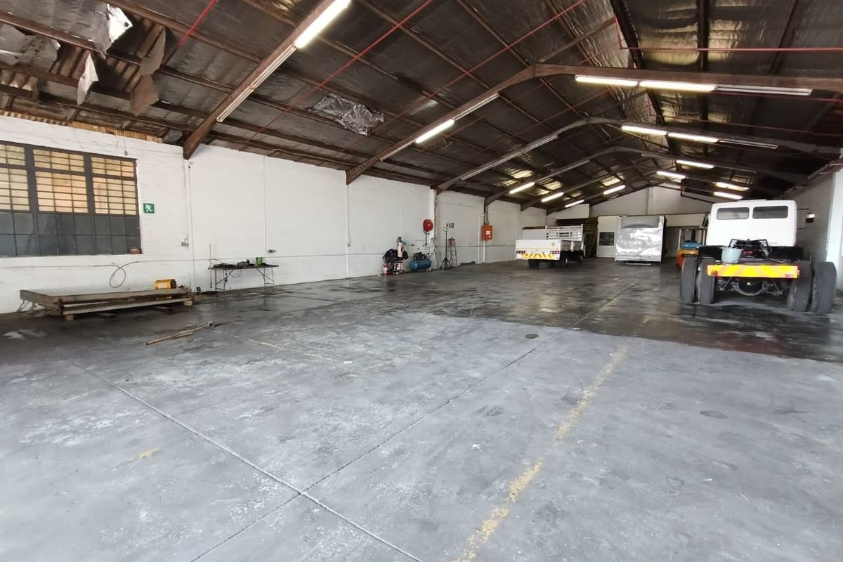 Spacious industrial warehouse featuring high ceilings with exposed steel trusses, concrete flooring, and large metal-framed windows, suitable for storage or workshop operations.