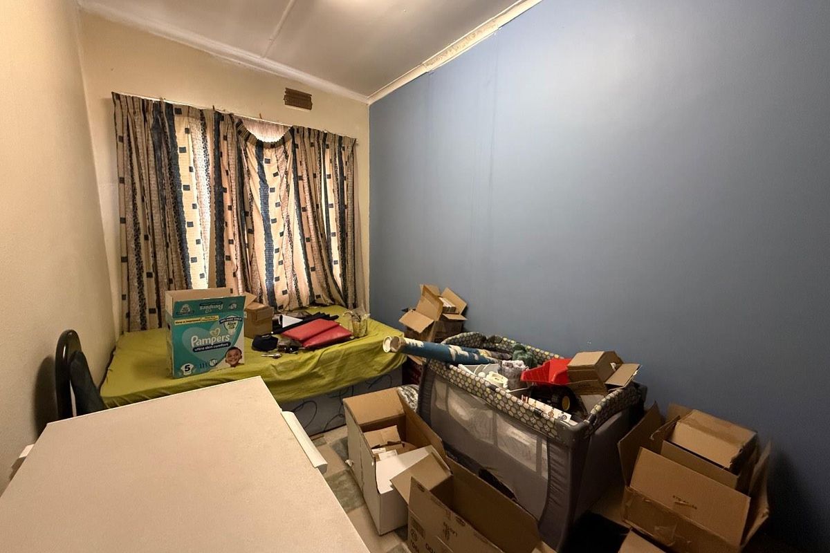 A bedroom featuring a window with curtains and painted walls, currently used for storage.