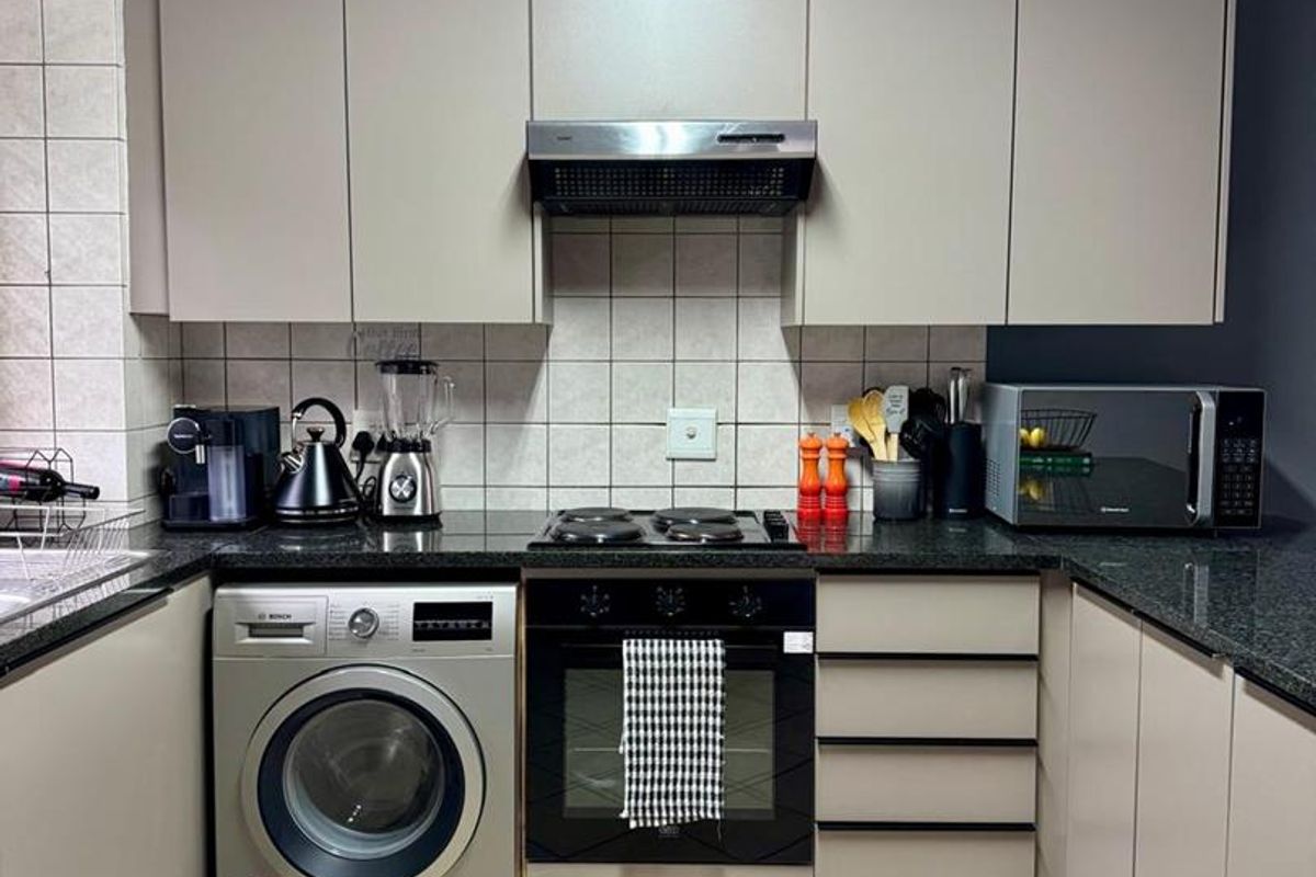 A functional kitchen featuring modern grey cabinetry, granite countertops, a built-in oven with hob, extractor fan, and integrated laundry appliance space.
