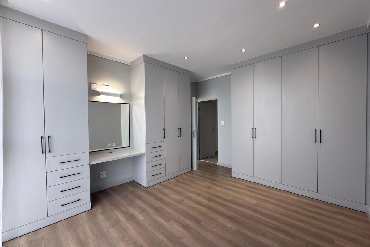 A modern bedroom featuring extensive built-in cabinetry with integrated vanity, recessed downlighting, and wood-look laminate flooring.