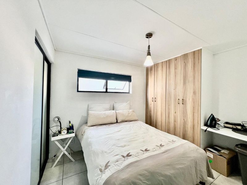 A well-maintained bedroom featuring built-in wooden cupboards, tiled flooring, a pendant light fixture, and a functional built-in desk area.