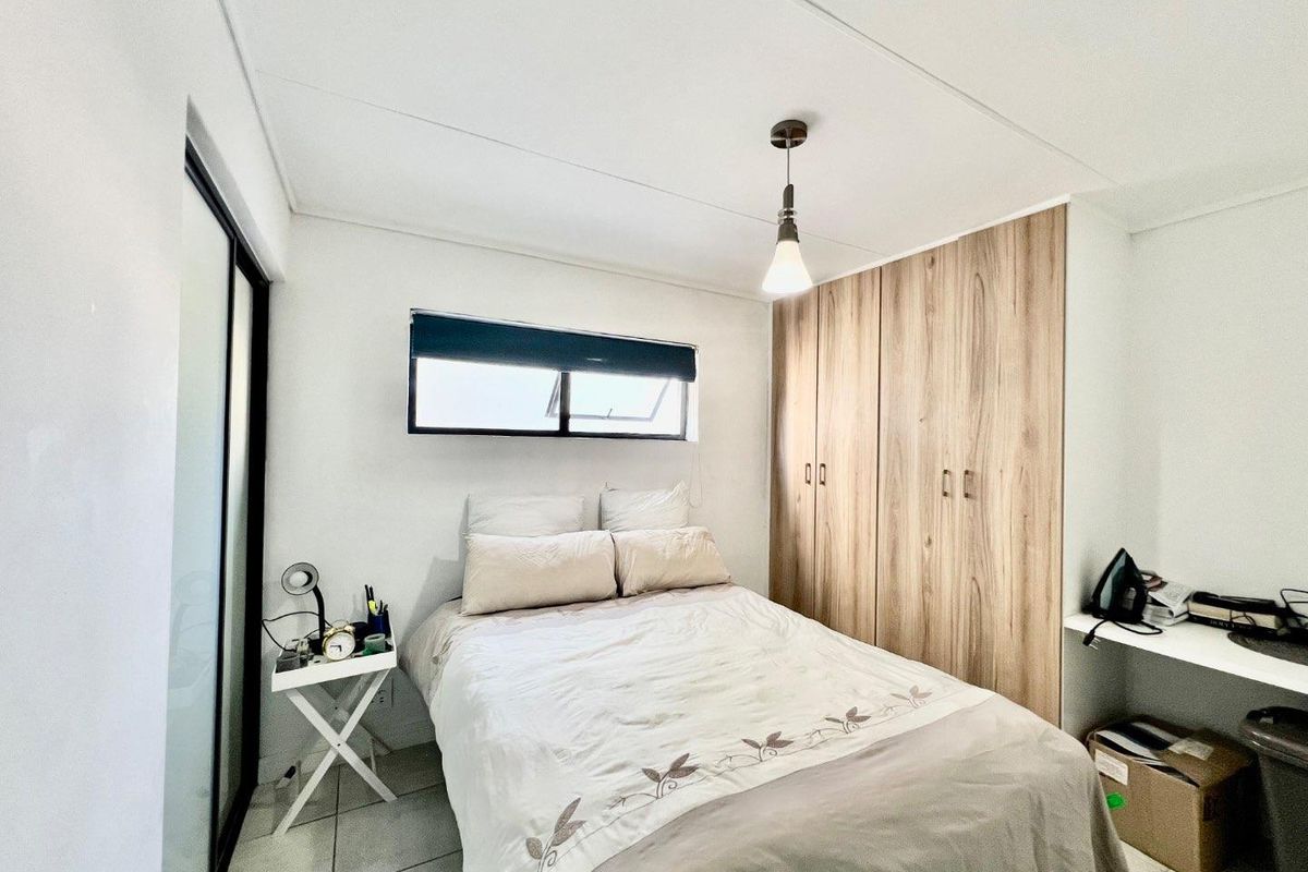A well-maintained bedroom featuring built-in wooden cupboards, tiled flooring, a pendant light fixture, and a functional built-in desk area.