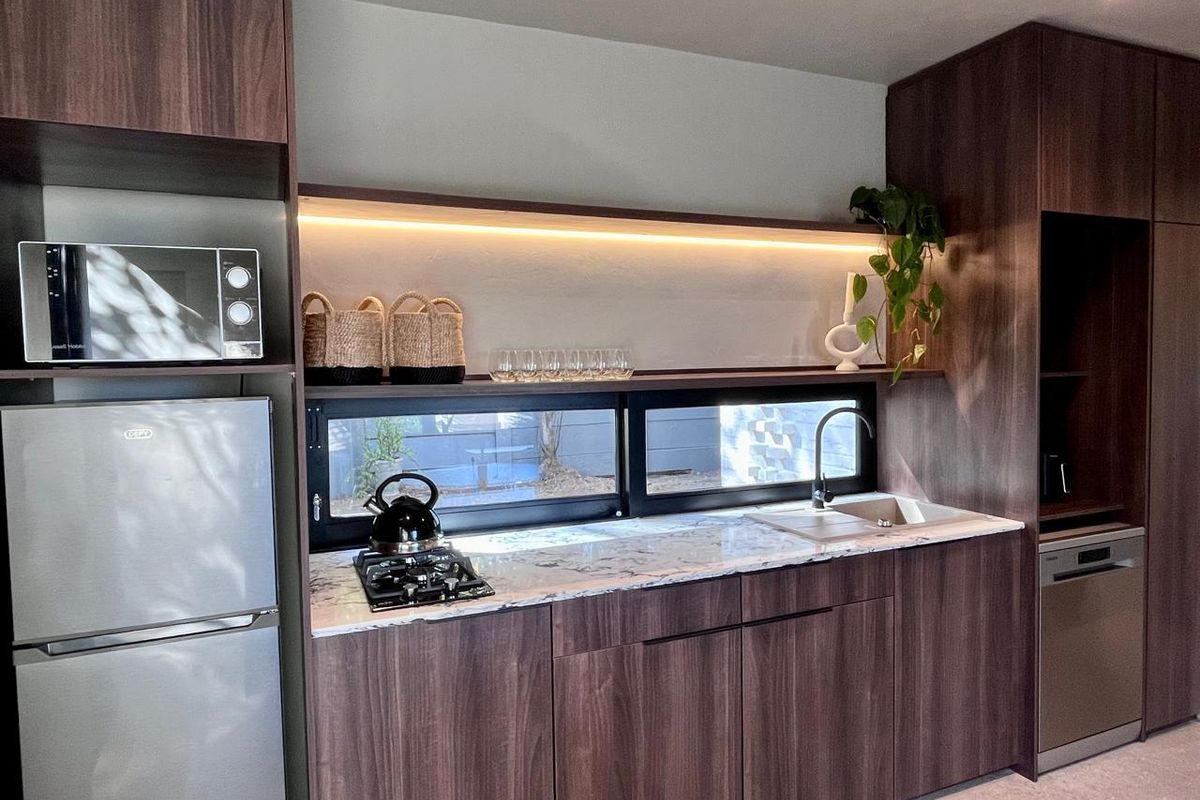 Modern kitchen featuring dark wood cabinetry, marble-look countertops, integrated appliances, and a sleek horizontal window with under-cabinet LED lighting.