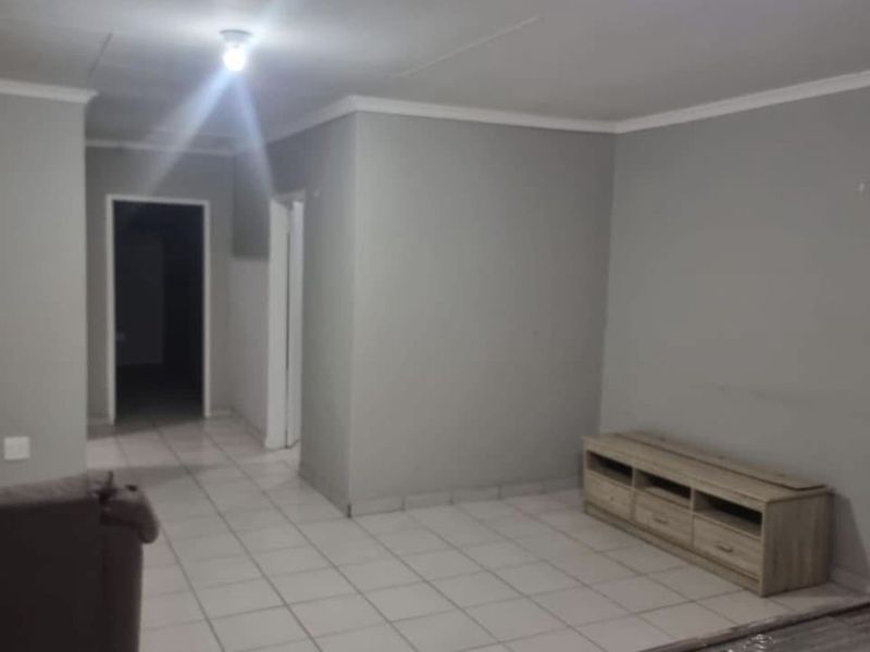 A neutrally painted living area featuring tiled flooring and coved ceilings, providing a clean and functional space with access to adjacent rooms.