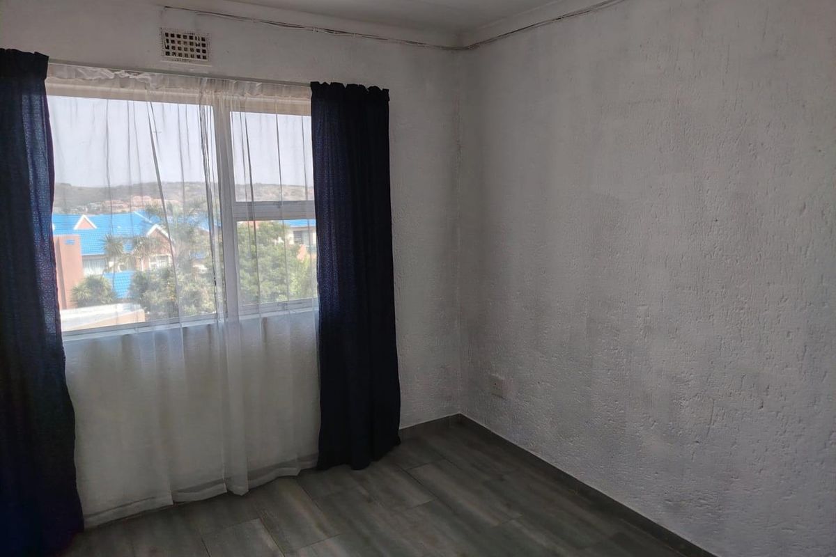 An empty bedroom featuring laminate flooring, textured walls, and a window with curtains, offering a blank canvas for potential interior updates.