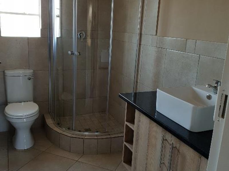 A clean, functional bathroom featuring a corner shower enclosure, a modern vessel sink on a vanity cabinet, and neutral floor-to-ceiling tiling.