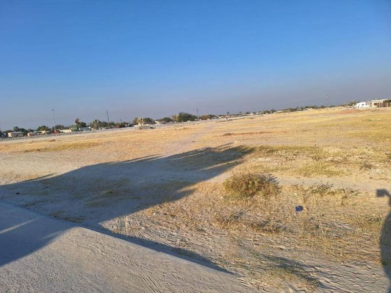 A wide-angle view of a vacant residential plot featuring flat, undeveloped land with sparse vegetation under a clear sky.