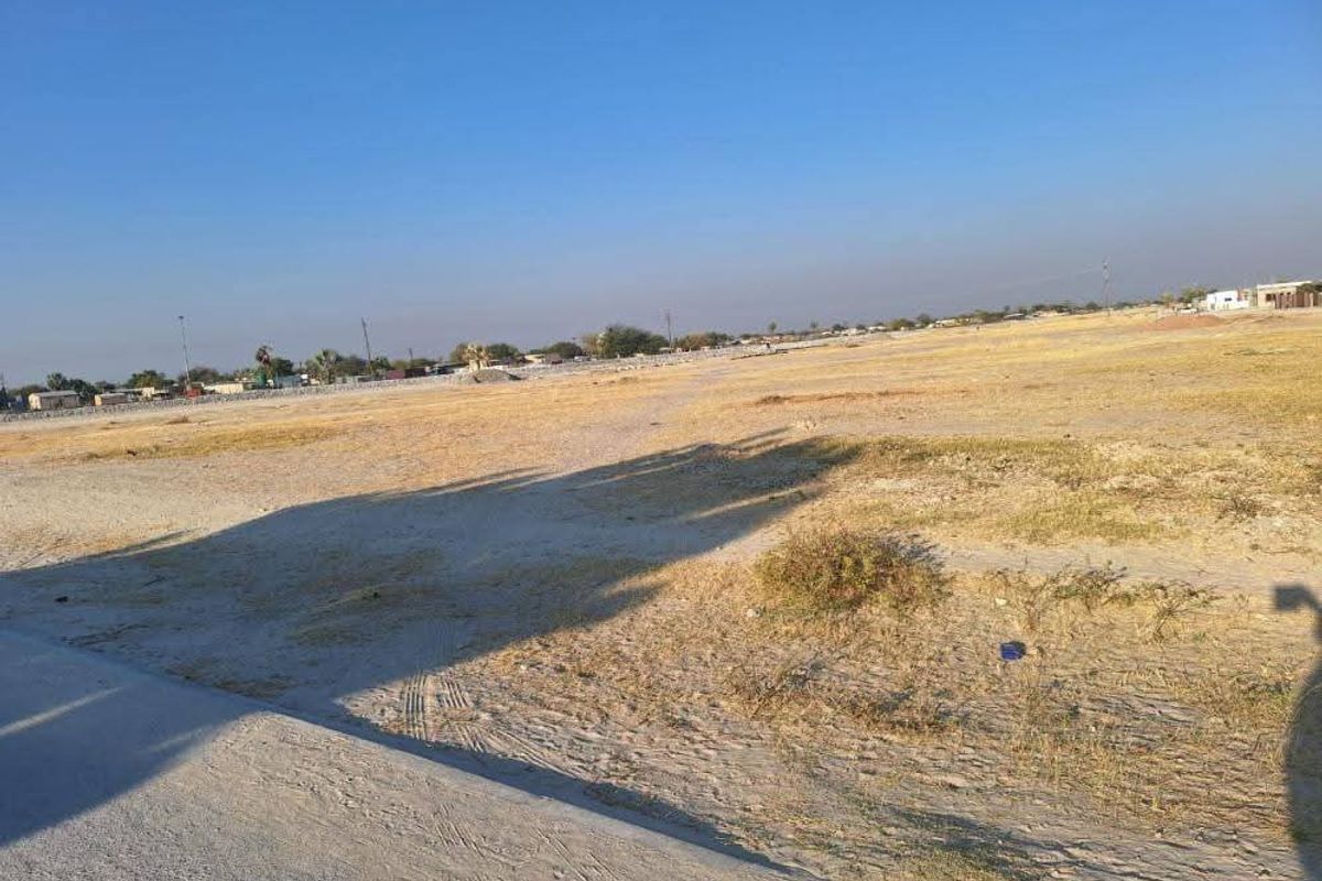 A wide-angle view of a vacant residential plot featuring flat, undeveloped land with sparse vegetation under a clear sky.