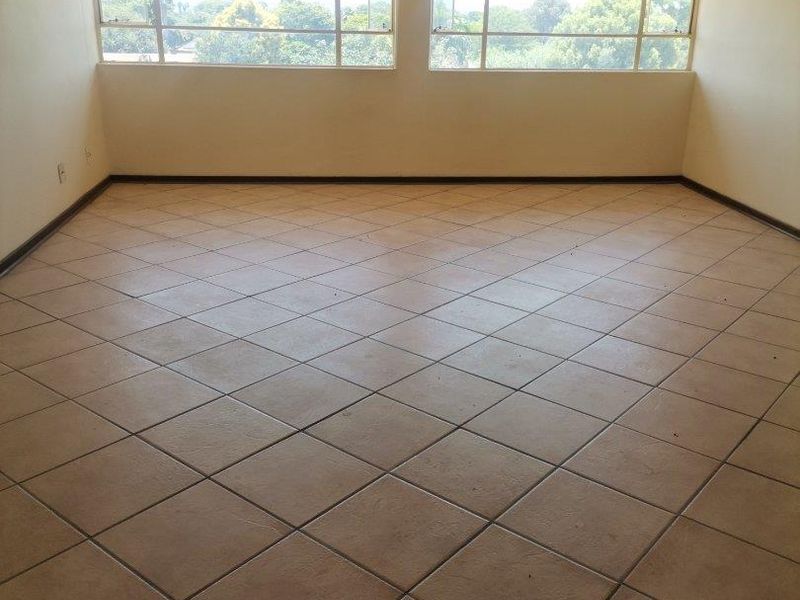 An empty living room featuring large windows with natural light and tiled flooring, offering a blank canvas for renovation or interior design.