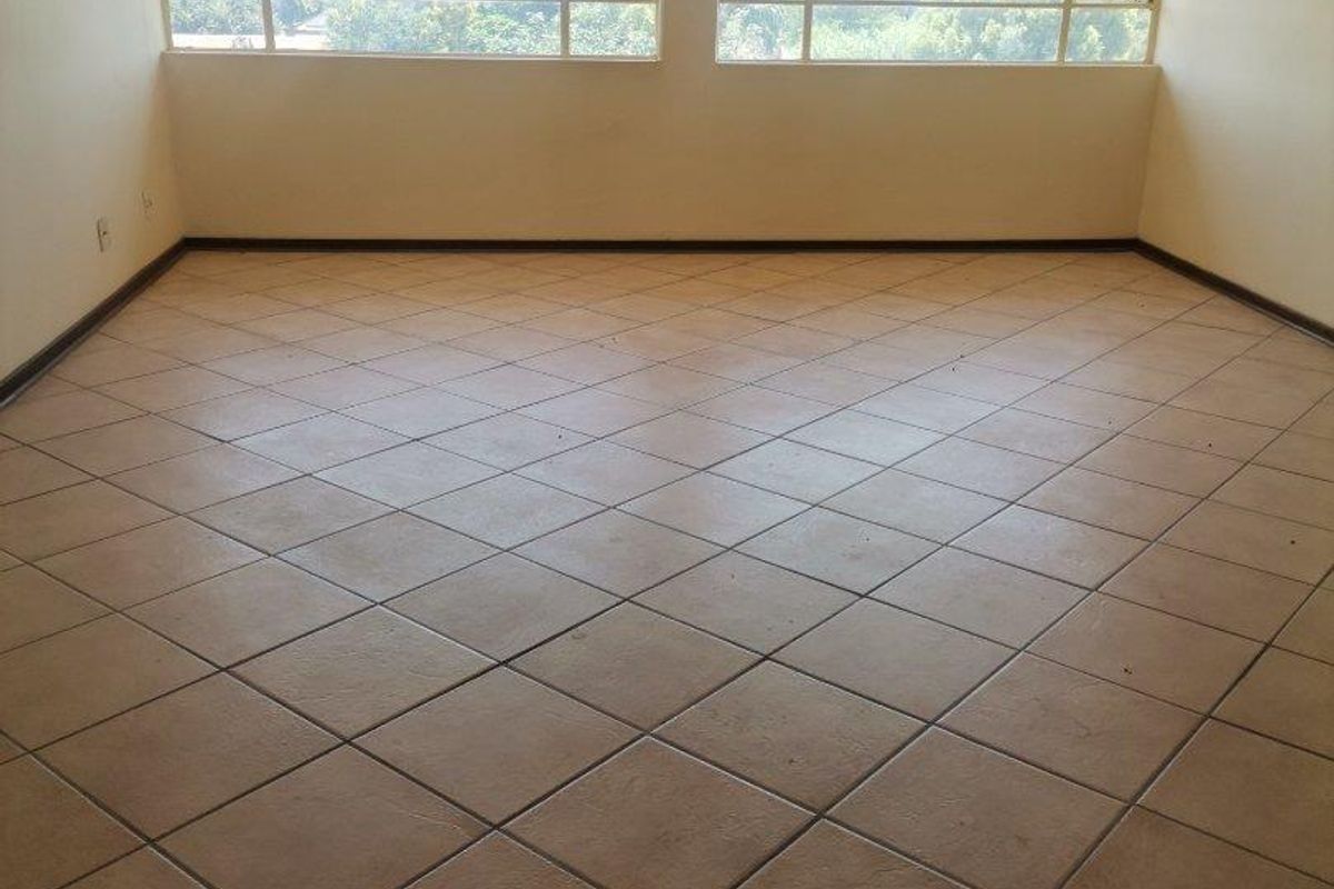 An empty living room featuring large windows with natural light and tiled flooring, offering a blank canvas for renovation or interior design.
