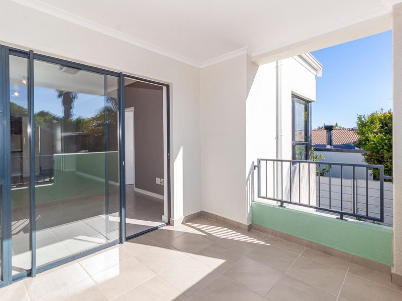 A clean, covered balcony featuring tiled flooring, a metal balustrade, and large sliding glass doors providing access to the interior living space.