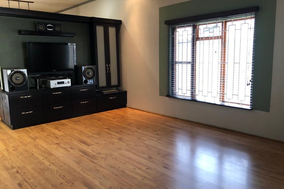 Spacious living room featuring laminate flooring, recessed lighting, and a large built-in media unit with integrated shelving.