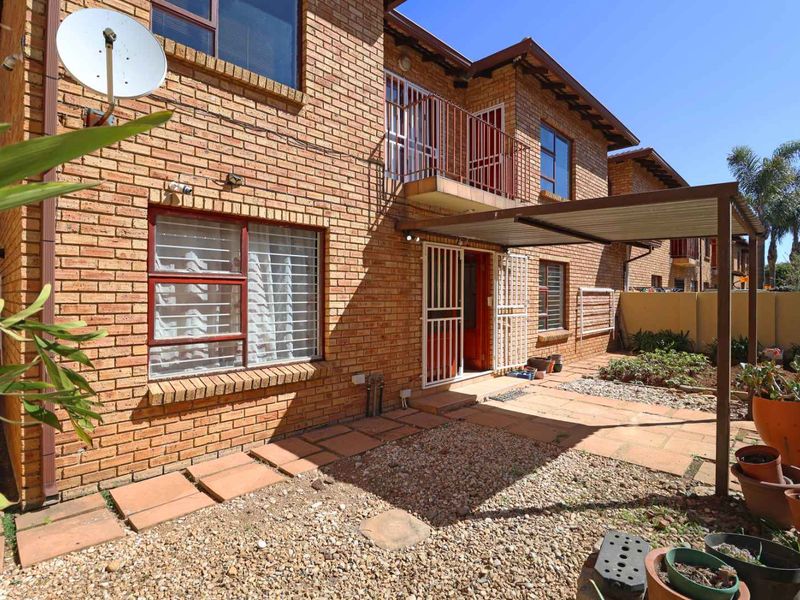 Rear view of a face brick townhouse featuring a covered patio, small gravel garden, and an upper-level balcony with metal railings.