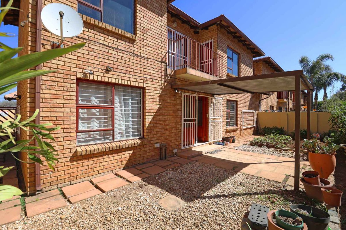 Rear view of a face brick townhouse featuring a covered patio, small gravel garden, and an upper-level balcony with metal railings.
