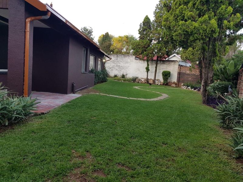 A well-maintained rear garden featuring a tiled patio area, established trees, and a secure boundary wall.