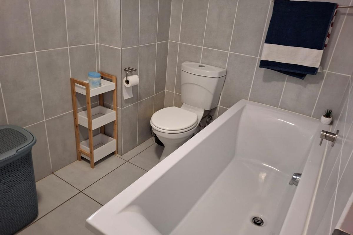 A clean, modern bathroom featuring full-height grey wall tiling, a white bathtub, and a standard toilet suite.