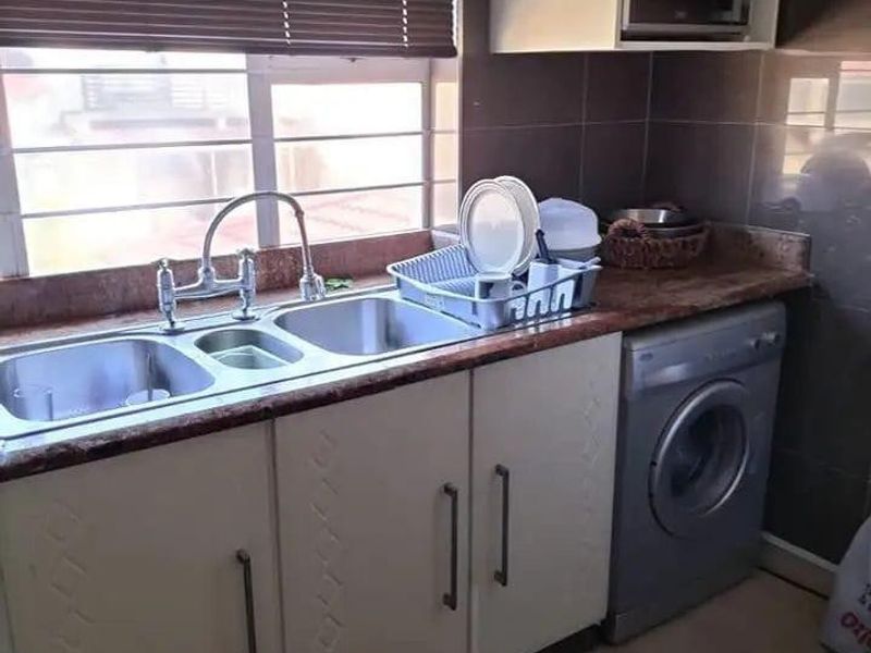A functional scullery area featuring built-in cabinetry, a double stainless steel sink, tiled backsplash, and space for a washing machine.