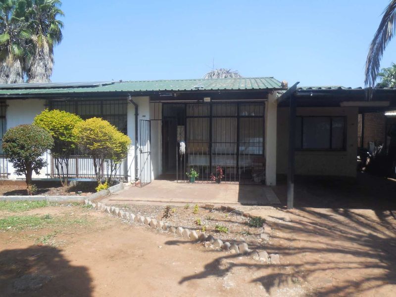 Front exterior view of a single-story house featuring a corrugated metal roof, security bars, and an attached carport area.