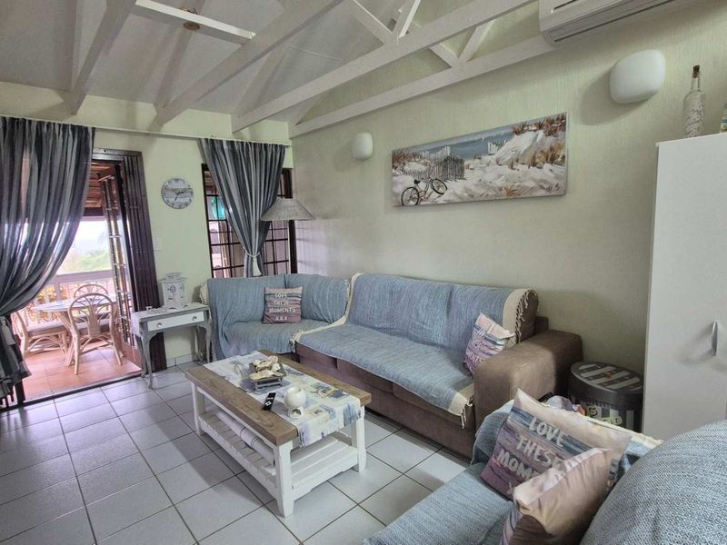 A living room featuring exposed timber rafters, tiled flooring, and a split-system air conditioner, with direct access to an outdoor patio area.