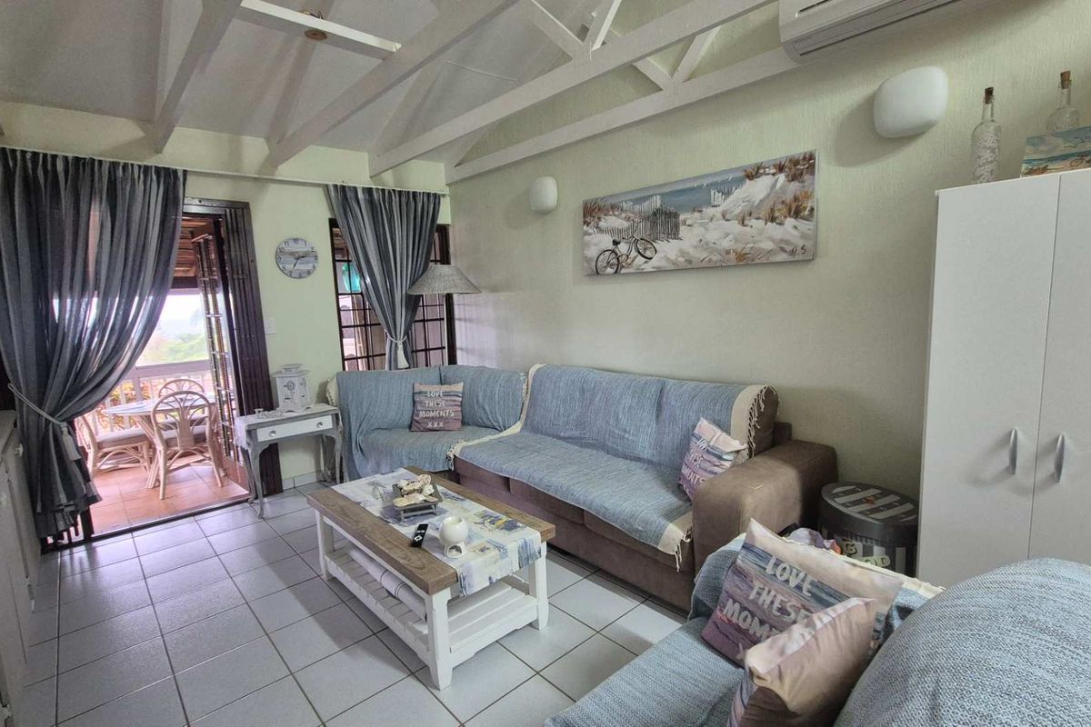 A living room featuring exposed timber rafters, tiled flooring, and a split-system air conditioner, with direct access to an outdoor patio area.