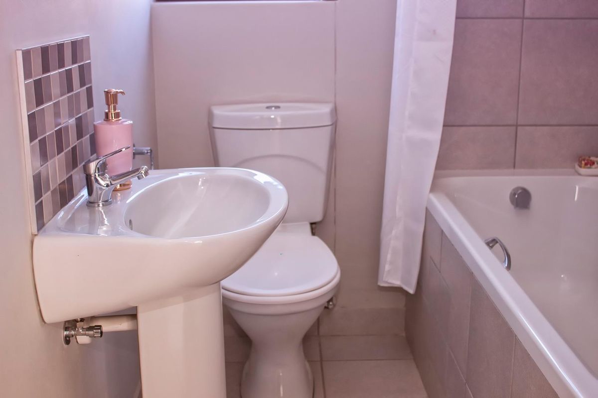 A functional bathroom featuring a pedestal basin, toilet, and bathtub with neutral wall and floor tiling.