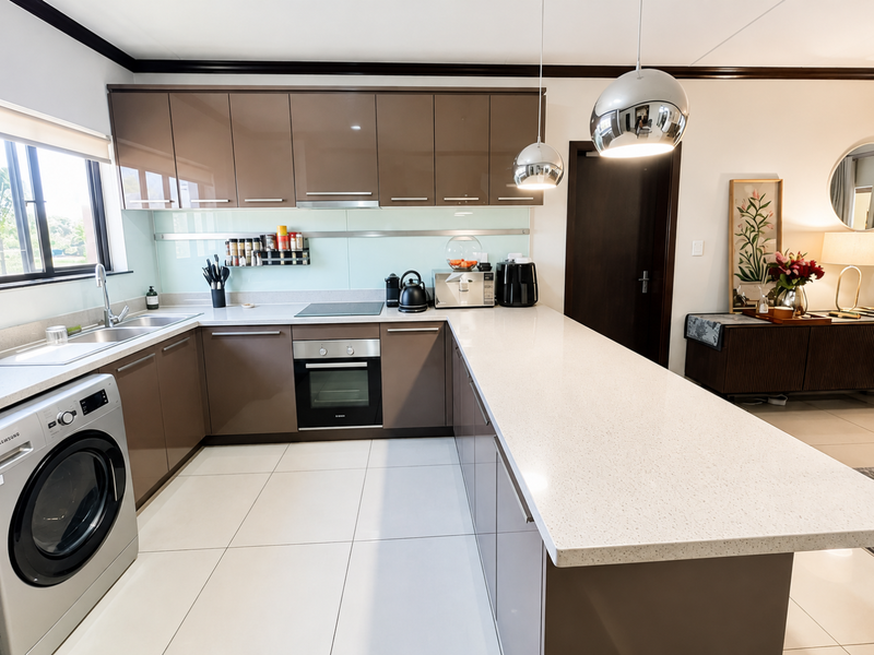 Modern kitchen featuring high-gloss brown cabinetry, stone countertops, integrated stainless steel oven, electric hob, and a spacious breakfast bar with pendant lighting.