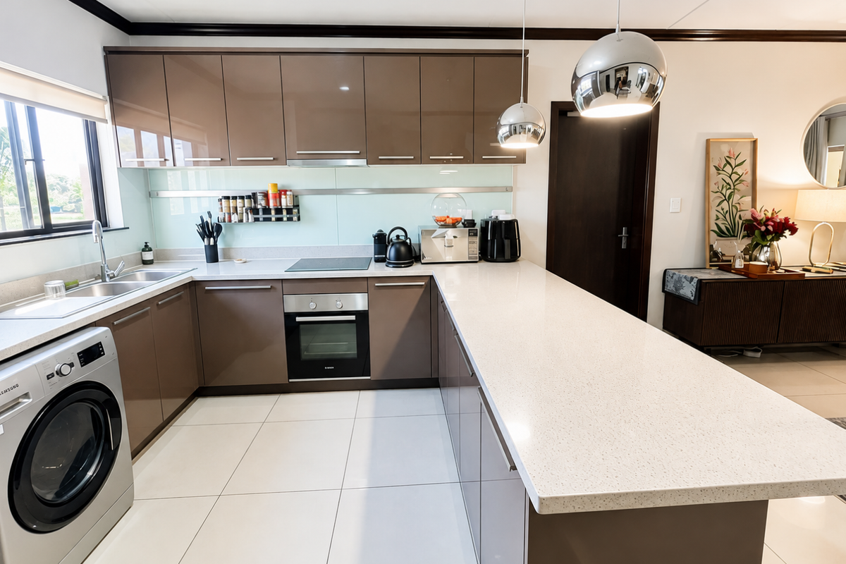 Modern kitchen featuring high-gloss brown cabinetry, stone countertops, integrated stainless steel oven, electric hob, and a spacious breakfast bar with pendant lighting.