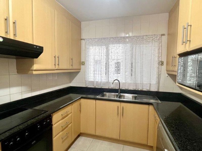 A functional kitchen featuring light wood-tone cabinetry, dark granite countertops, a double sink, and integrated cooking appliances with a tiled backsplash.