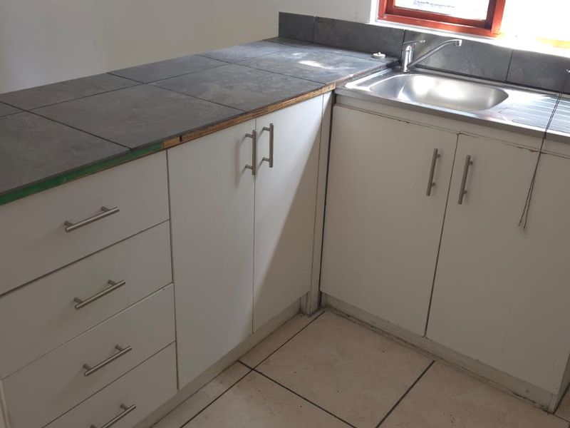 A compact kitchen area featuring white built-in cabinetry, a stainless steel sink, and tiled countertops, presenting a functional space ready for updates.