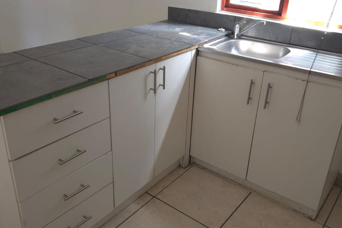 A compact kitchen area featuring white built-in cabinetry, a stainless steel sink, and tiled countertops, presenting a functional space ready for updates.