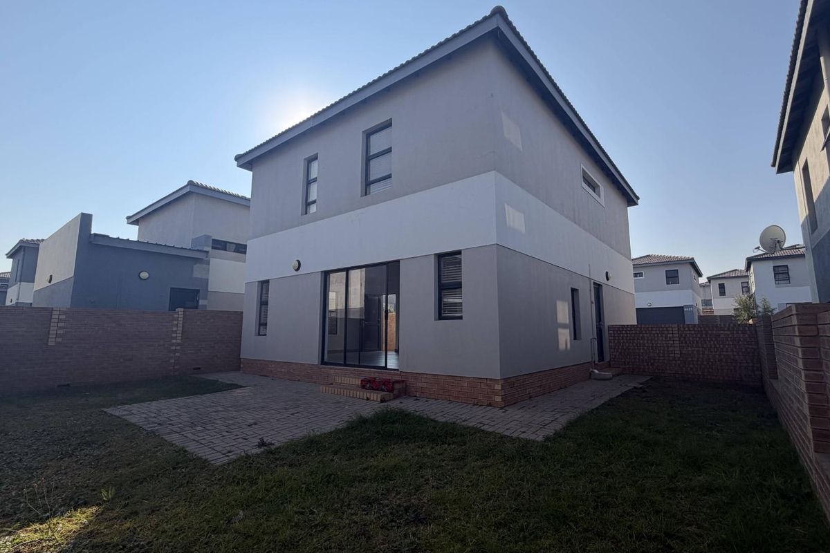 Rear view of a modern two-story house featuring a paved patio area, brick boundary walls, and a private garden space.