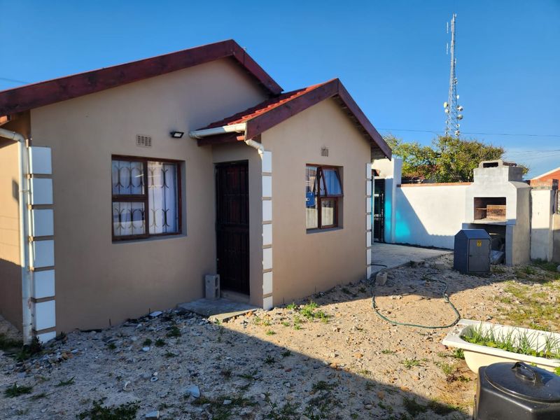 Rear view of a single-story house featuring a built-in braai, security gates, and an unlandscaped yard area.