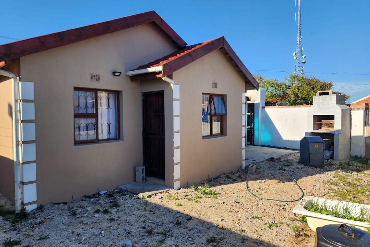Rear view of a single-story house featuring a built-in braai, security gates, and an unlandscaped yard area.