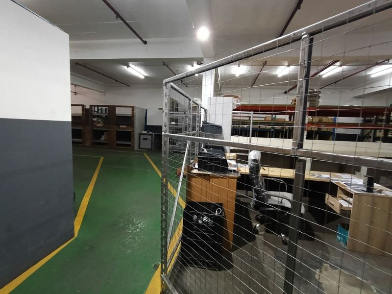 Industrial utility space featuring epoxy flooring, exposed ceiling infrastructure, wire mesh partitioning, and integrated industrial shelving units.