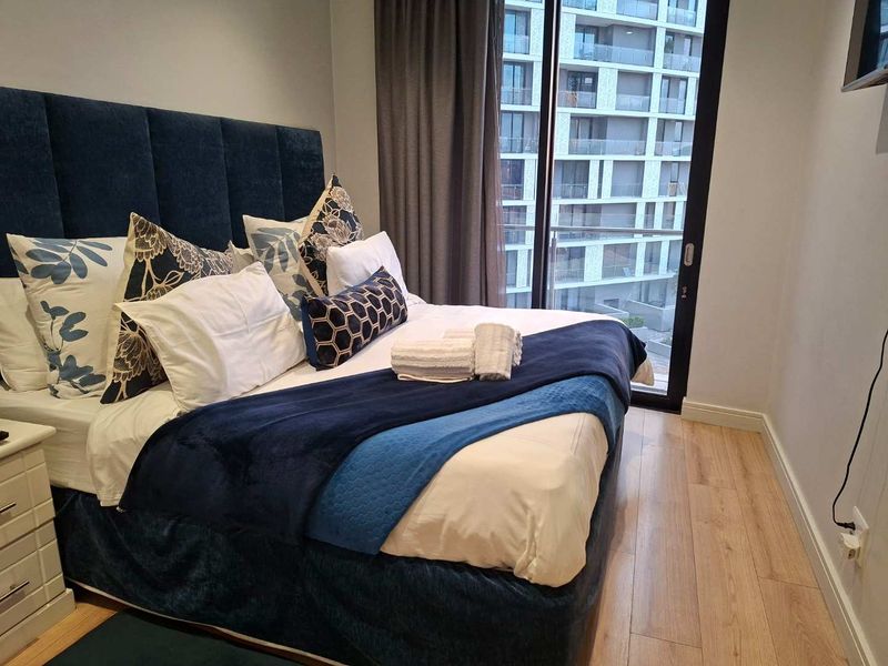 A well-maintained bedroom featuring laminate flooring and a sliding glass door providing access to a balcony with urban views.