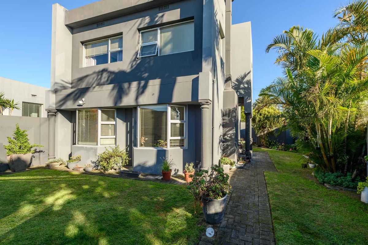 Rear view of a modern two-story house featuring a paved walkway, manicured lawn, and large aluminium-framed windows.