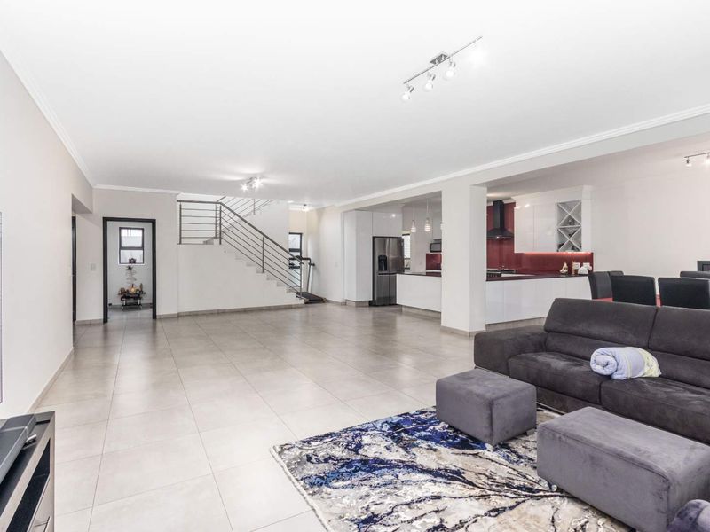 Spacious open-plan living area featuring large format floor tiles, a modern staircase with metal balustrades, and a contemporary kitchen with integrated cabinetry.