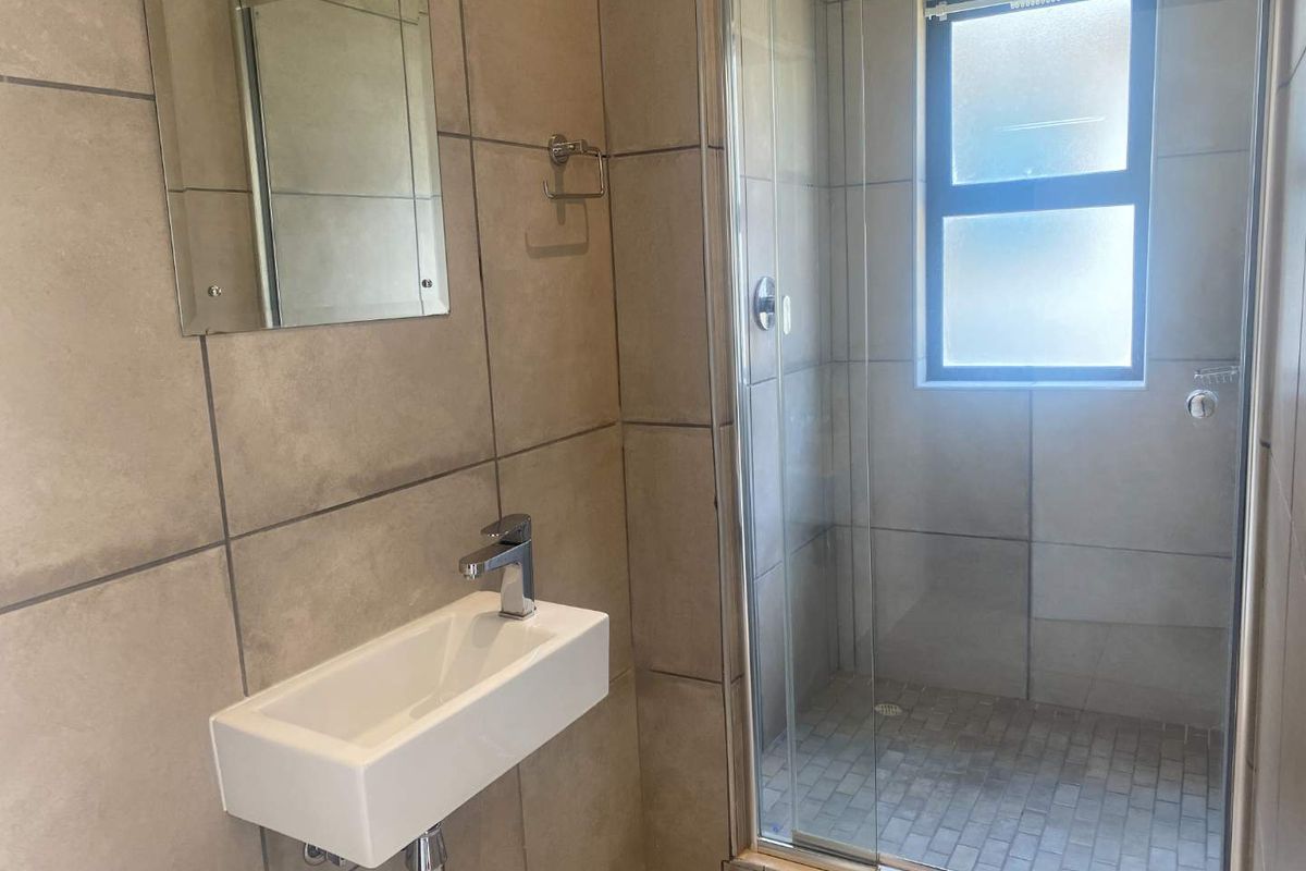 A modern bathroom featuring a wall-mounted basin, a glass-enclosed shower, and neutral floor-to-ceiling tiling.