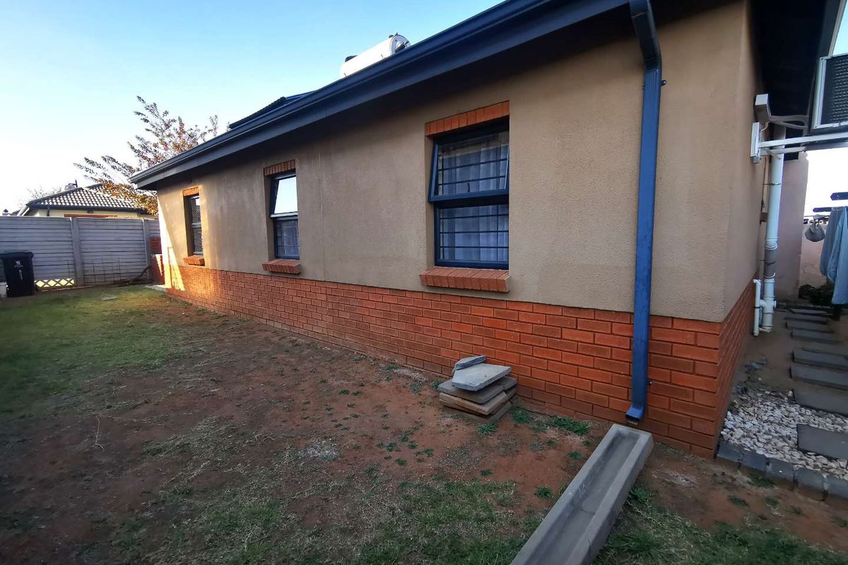 Rear exterior view of the house featuring a combination of brick and plastered walls, security-fitted windows, and a solar geyser installation.