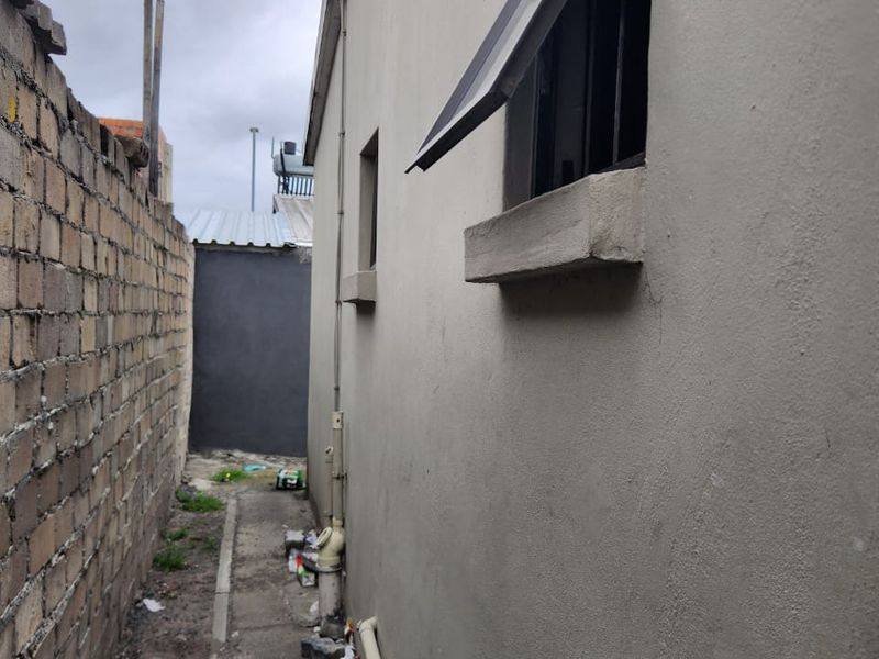 A narrow side passage of the house featuring a concrete pathway, boundary wall, and external plumbing fixtures along the exterior wall.