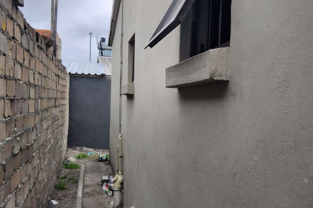 A narrow side passage of the house featuring a concrete pathway, boundary wall, and external plumbing fixtures along the exterior wall.