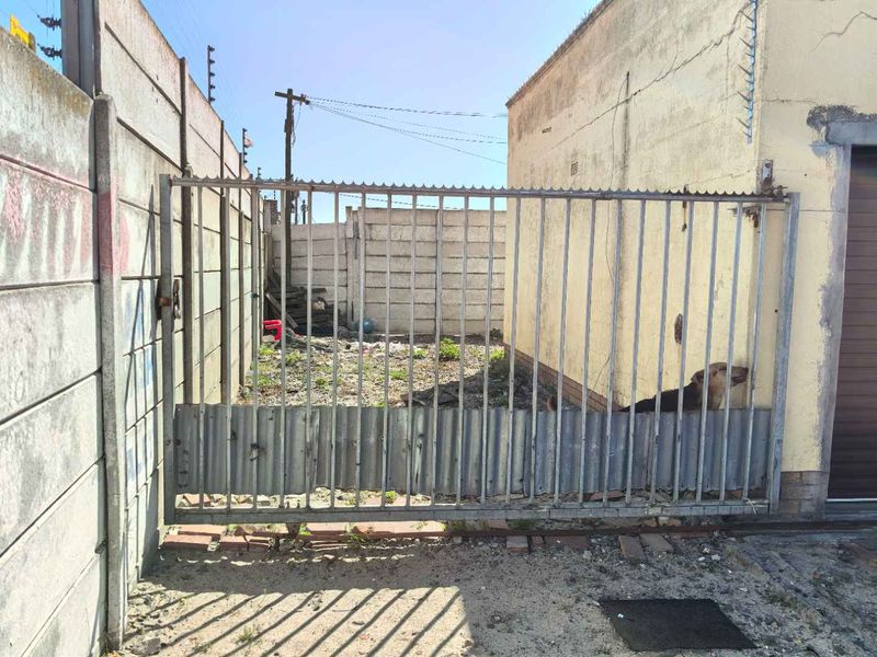 Rear exterior view of the property featuring a metal sliding gate and precast concrete boundary walls with visible signs of weathering and wear.