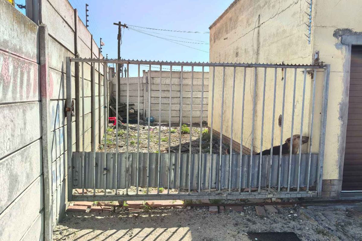 Rear exterior view of the property featuring a metal sliding gate and precast concrete boundary walls with visible signs of weathering and wear.