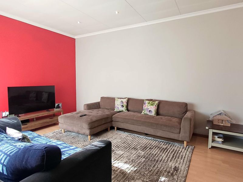 A living room featuring laminate flooring and recessed downlights, with a bold red accent wall.