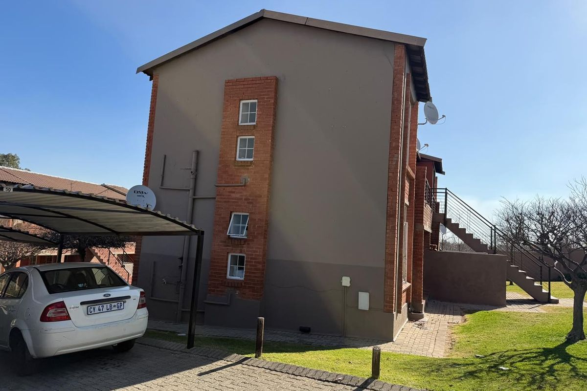 Side and rear view of a multi-story apartment building featuring brick and plaster finishes, external staircase access, and a covered carport.