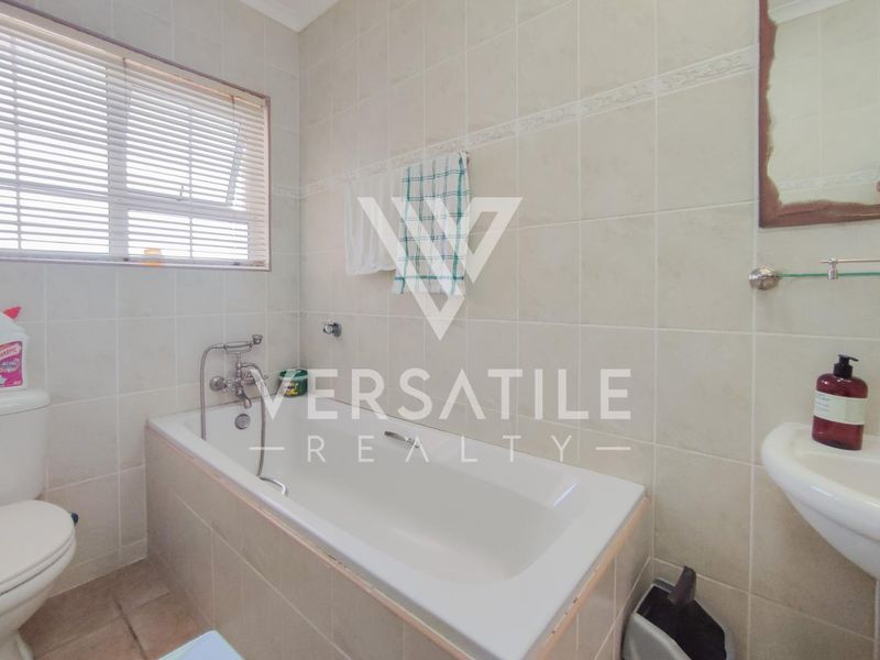 A functional bathroom featuring a bathtub, wall-mounted basin, and toilet, finished with neutral wall and floor tiles.