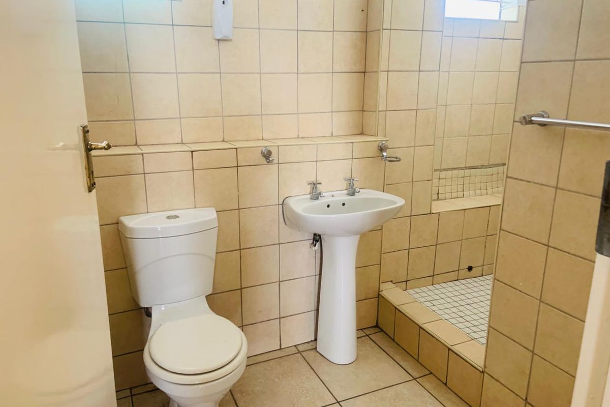 A functional bathroom featuring a pedestal basin, toilet, and a tiled shower cubicle with neutral wall and floor tiling.