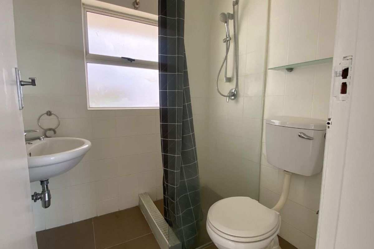 A functional bathroom featuring a wall-mounted basin, a shower with a glass screen, and a standard toilet, finished with neutral wall and floor tiles.