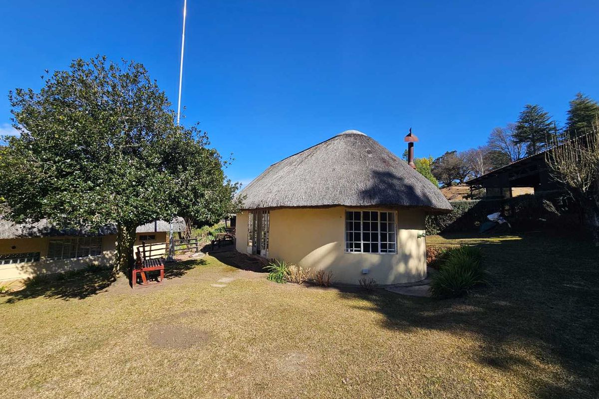 A charming round cottage with a traditional thatched roof and plastered walls, set within a well-maintained garden area on the farm property.